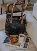 Cartera negra de cuero con doble asa marrón, bolsillo externo y cierre superior.