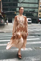 Vestido midi color beige con detalles de encaje marrón, cuello alto con lazo, escote pico, manga larga y botones frontales.