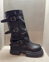 Bota negra de caña media con suela track y tres correas con hebillas plateadas.