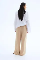 Pantalón de punto color beige, de corte holgado con piernas amplias, tiro alto, cintura elástica y cordón para ajustar.