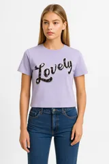 Remera lila de algodón con cuello redondo y estampado frontal con la palabra "Lovely" en letras negras con relleno floral.