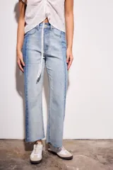 Jean de tiro medio, corte recto y largo cropped, confeccionado en denim de algodón con elastano. Presenta un efecto de lavado bicolor o combinado, con paneles de diferente tono de azul claro, y costuras verticales marcadas en el frente. El ruedo es deshilachado.