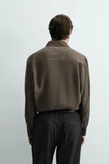 Camisa relaxed fit color verde militar, confeccionada en tejido con mezcla de modal. Tiene cuello solapa, manga larga con puño abotonado, bolsillo plastrón en el pecho y cierre frontal de botonadura.