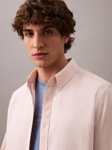 Camisa de manga larga color rosa claro, confeccionada en tejido Oxford de algodón y elastano. Presenta cuello camisero clásico, cierre frontal con botones y logo de Calvin Klein bordado en el pecho. Corte regular.