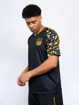 Remera de entrenamiento del Club Atlético Peñarol, color negro con detalles geométricos en amarillo y gris en las mangas y cuello. Escudo del club bordado en el pecho.