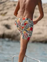 Short de baño blanco con estampado de hojas de palmera en tonos verde, rojo y amarillo.
