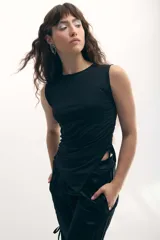 Musculosa negra con cuello redondo y corte asimétrico con jaretas laterales regulables que permiten ajustar el largo y el volumen.