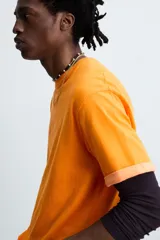 Camiseta naranja de algodón con cuello redondo y manga corta con vuelta. Estampado frontal con la firma del artista Otis Kwame Kye Quaicoe.