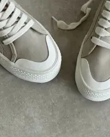 Zapatillas urbanas de lona color beige con cordones blancos y suela de goma blanca con diseño geométrico.