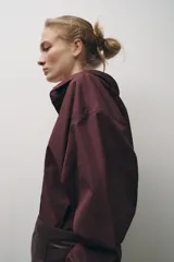 Camisa color borgoña de Zara Woman Collection, confeccionada en algodón popelín. Tiene cuello solapa, escote en pico, mangas largas con puños abotonados, bajo redondeado y cierre frontal con botones.