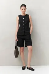 Bermuda negra de tiro medio con silueta recta y largo a la altura de la rodilla. Presenta bolsillos laterales y traseros, y costuras visibles.
