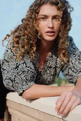 Blusa de popelina de algodón con estampado de hojas en blanco y negro. Tiene cuello mao, abertura en V con botones y mangas globo tres cuartos con puños finos.