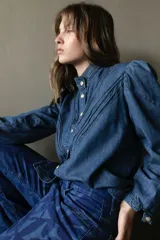 Camisa gris de jean liviano con cuello mao, cierre frontal con botones dorados, mangas 3/4 con puños fruncidos y detalle de costuras horizontales en el pecho.