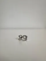 Anillo plateado de acero quirúrgico hipoalergénico con diseño irregular y aberturas circulares.