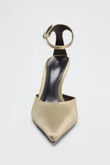 Zapato de tacón color dorado con acabado satinado, punta fina y pulsera al tobillo con hebilla metálica.
