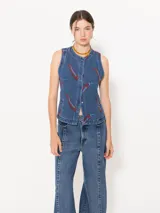 Chaleco denim azul con estampado de pimientos rojos, cuello redondo, pinzas de entalle, bolsillos sastreros y cierre frontal con broches.