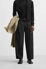 Pantalón negro de corte amplio tipo balloon fit, con cintura con pliegues frontales, bolsillos delanteros y traseros de plastrón. Cierre frontal con cremallera y botón.