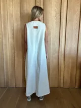 Vestido largo color crudo, sin mangas y con escote en V. Presenta aberturas laterales en el ruedo y bolsillos laterales a la altura de la cadera.