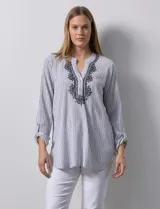 Blusa de gasa bambula a rayas verticales celestes y blancas, con cuello a la base, escote en V con botones y bordado floral negro. Mangas largas regulables con presilla y botón.