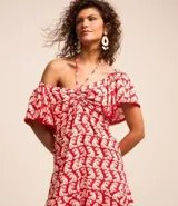 Vestido corto de viscosa y lino con estampado de olas en color blanco sobre fondo rojo. Tiene escote off-shoulder, mangas cortas holgadas, lazo en el busto con detalle de abalorios y volado en el bajo.
