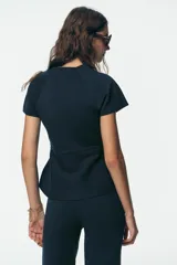 Top azul marino de punto con cuello redondo y manga corta. Tiene corte a la cintura y peplum en el bajo.