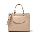 Cartera estructurada mediana color beige claro (hueso) de material símil cuero (PU) con forrería textil. Presenta doble manija fija, correa larga regulable y desmontable, solapa frontal con botón imantado y cierre superior con cremallera metálica.