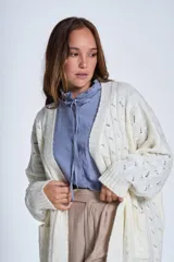 Sacón de hilado frizado color crudo, con calado delicado y bolsillos tejidos al frente. De corte relajado.