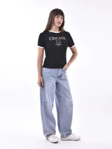 Remera negra de manga corta con cuello redondo y ribete blanco. Presenta un estampado frontal con el texto "CHICAGO" en blanco, un logo circular con una "M" en el centro y el texto "CULTURAL WIND CITY SINCE 2023" debajo.