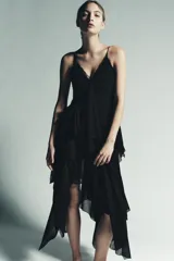 Vestido midi negro, con escote pico adornado con encaje a tono y tirantes finos. Presenta una cascada de volantes en la parte delantera y un bajo asimétrico.