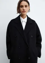 Abrigo largo negro oversize con doble botonadura, solapas con muesca, hombros caídos, bolsillos laterales y abertura posterior.