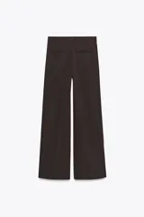 Pantalón marrón de tiro alto con trabillas, doble pliegue, bolsillos laterales y de vivo en la espalda, pernera ancha y cierre frontal con cremallera y gancho metálico.