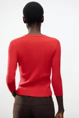 Chaqueta de punto roja con escote en pico, manga francesa y cierre frontal con botones dorados.