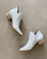 Botín de cuero vacuno color blanco, con puntera fina y caña baja con aberturas laterales. Presenta detalle de calado en el empeine y taco de madera.
