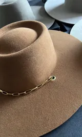 Sombrero de ala ancha color marrón, con copa alta y ala recta. Incluye cadena dorada decorativa. Hecho en lana merino uruguaya.