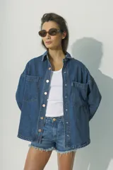 Camisa de denim azul con botones dorados, corte holgado, cuello clásico y bolsillos frontales.