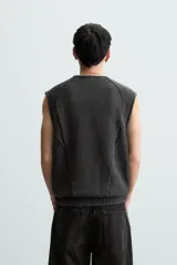 Chaleco negro de punto con cuello en V y cierre frontal con cremallera. Tiene bolsillos de ribete en la cadera y un corte relajado.