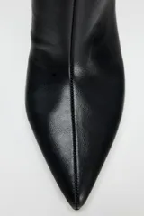 Bota negra de caña alta, confeccionada en cuero sintético, con terminación en punta y tacón fino.