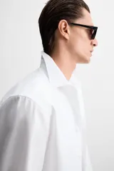Camisa blanca de algodón, corte slim fit, cuello italiano, manga larga con puños abotonados y cierre frontal con botones.