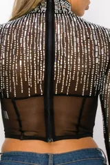 Top tipo corset de tul elastizado semi transparente color negro, con cuello alto y mangas largas. Cubierto con pedrería plateada.