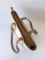 Bolso tipo tote bag color beige con laterales estampados y detalles en cuero marrón.