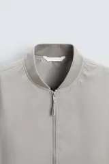 Cazadora bomber ligera gris confeccionada en tejido técnico. Cuello y puños en rib elástico, manga larga, bolsillos de vivo en cadera y bolsillo interior. Cierre frontal con cremallera.