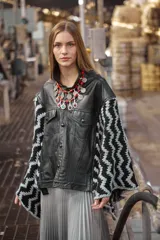 Poncho de cuero ovino negro con corte de chaqueta y mangas tejidas en lana con diseño geométrico en blanco y negro.