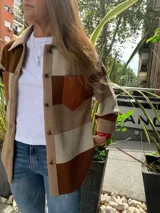 Camisa marrón con bloques de color beige y marrón oscuro. Presenta cuello camisero, cierre frontal con botones y un bolsillo de cuero en el pecho.