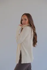 Sweater color crema de corte recto con cuello alto y aberturas laterales.