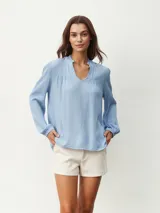 Blusa celeste con cuello mao y escote en V, de mangas largas con puños elásticos.