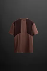 Camiseta deportiva marrón de corte relaxed fit, cuello redondo y manga corta. Presenta paneles laterales de malla negra y logo estampado en la espalda.
