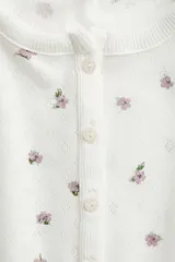 Top de manga corta en punto pointelle blanco con estampado floral diminuto en tonos rosados. Presenta cuello redondo con tapeta de botones.