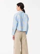 Camisa celeste con estampado floral, confeccionada en poplin con acabado paper touch, acceso mediante cartera oculta con botones y dos bolsillos plaque en el frente.