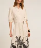 Vestido chemise evasé midi de viscolino color crema, con mangas abullonadas cortas, cuello camisero, botones delanteros, cinturón tejido para lazo en la cintura y bajo fruncido con estampa de palmeras y follaje.