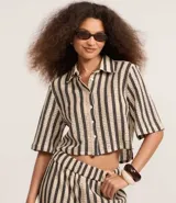 Camisa corta de algodón a rayas verticales color beige y negro, con cuello clásico, manga corta y cierre frontal con botones.